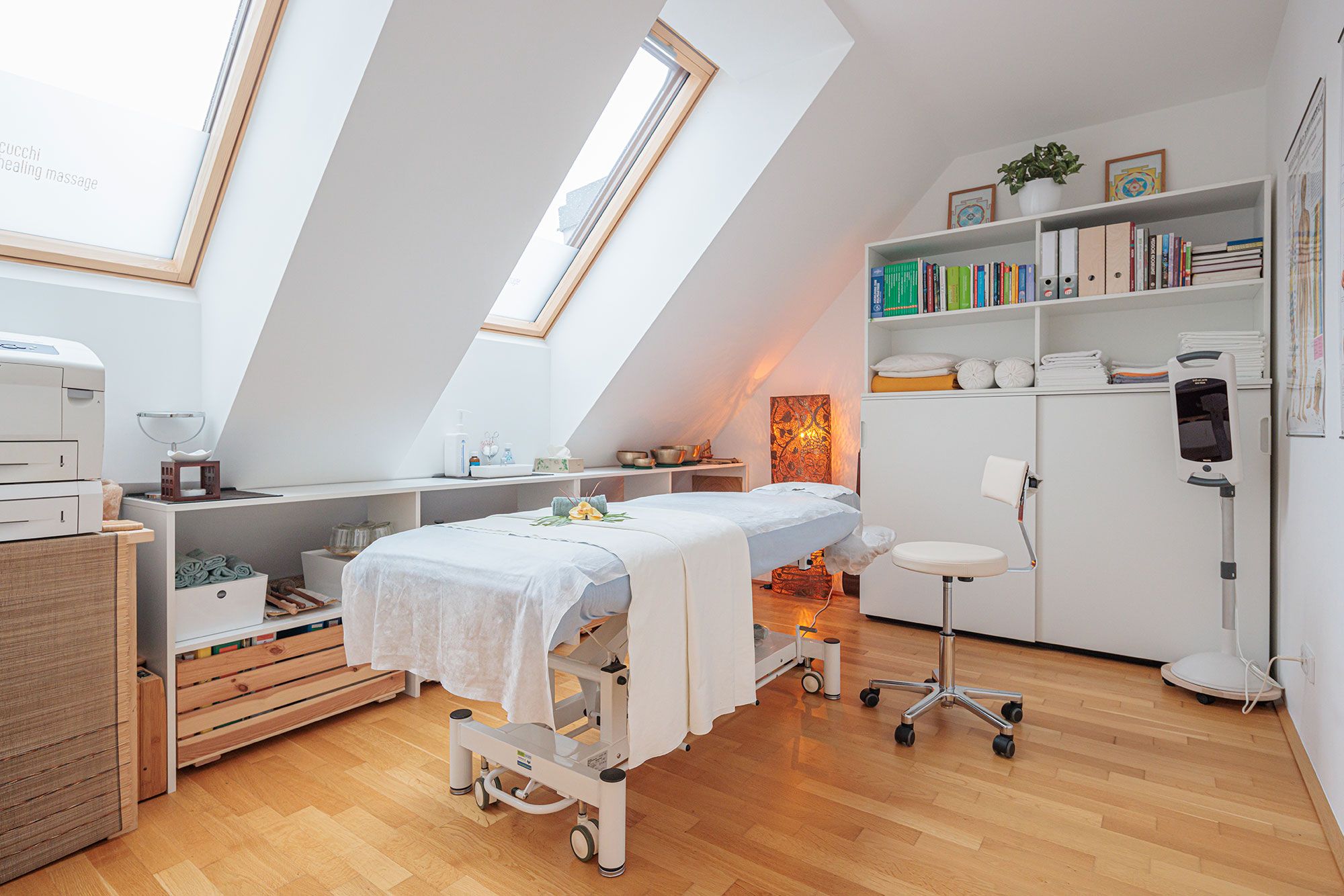 Heller Behandlungsraum im Dachgeschoß mit professioneller Massageliege, Infrarotlampe und Arbeitsmaterialien