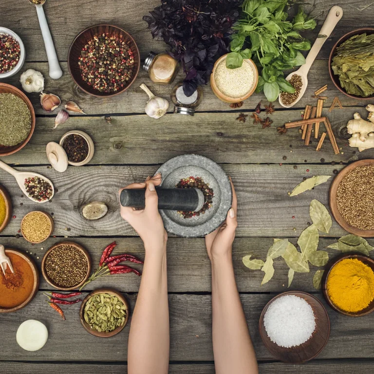 Hände zermahlen Kräuter und Gewürze mit einem Mörser auf einem Holztisch