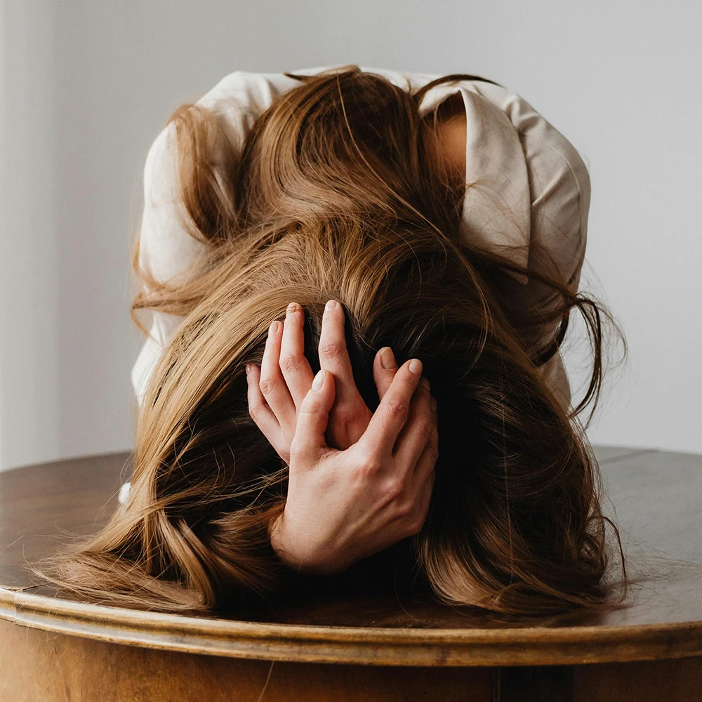 Frau sitzt nach vorne gebeugt mit Händen am Kopf