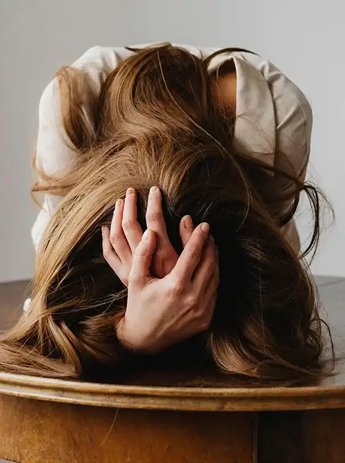 Frau sitzt nach vorne gebeugt mit Händen am Kopf