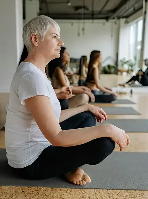 Frau sitzt achtsam auf einer Yogamatte im Gruppenraum