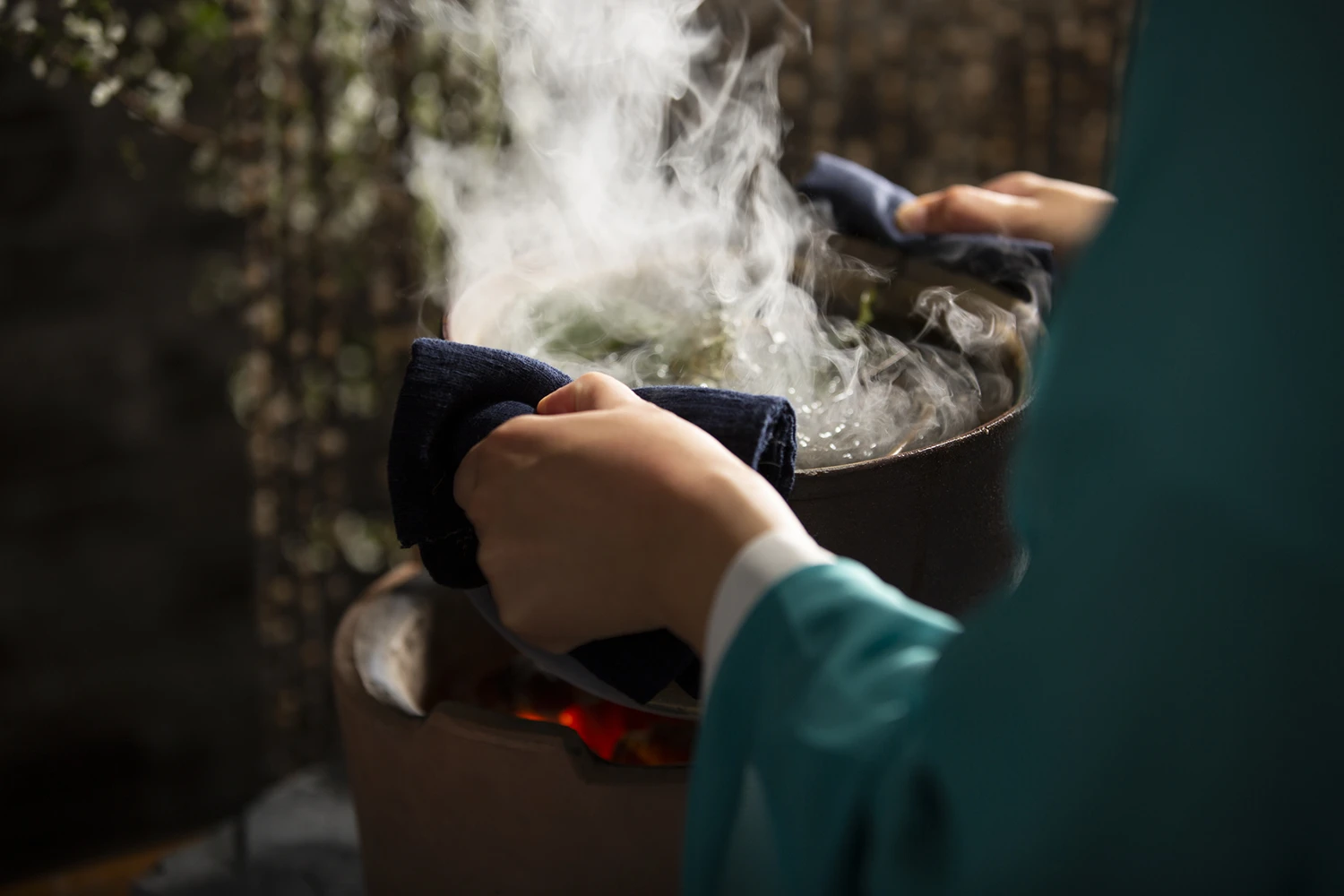 Hände halten einen dampfenden Topf mit Kräutersud über einer Wärmequelle, aufsteigender Dampf bei der Vorbereitung für Yoni Steaming